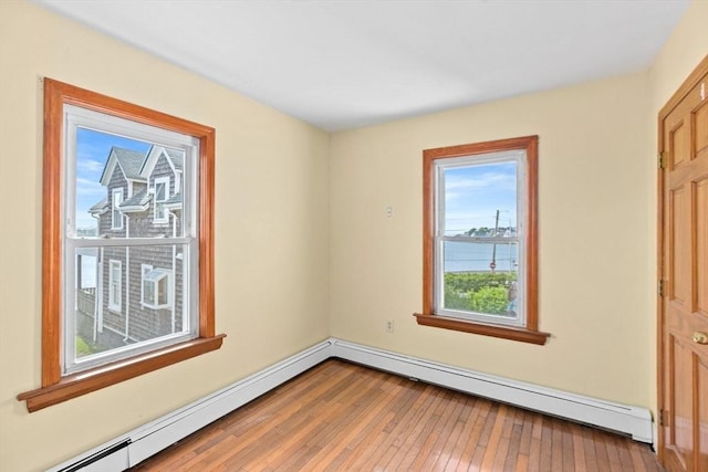 unfurnished room featuring a baseboard radiator, a water view, and wood finished floors