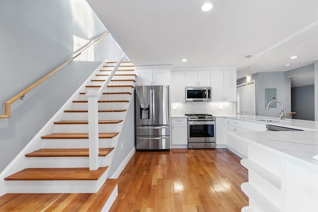 kitchen with decorative light fixtures, white cabinetry, appliances with stainless steel finishes, and light hardwood / wood-style flooring