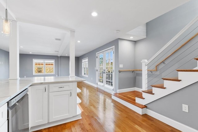 kitchen with decorative columns, stainless steel dishwasher, light hardwood / wood-style floors, white cabinetry, and hanging light fixtures