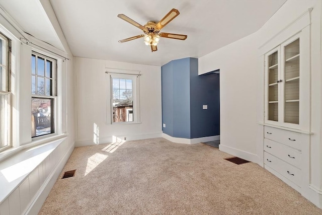 empty room with ceiling fan, carpet floors, visible vents, and baseboards