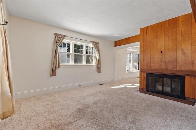 unfurnished living room featuring wooden walls, baseboards, visible vents, a fireplace with flush hearth, and carpet flooring