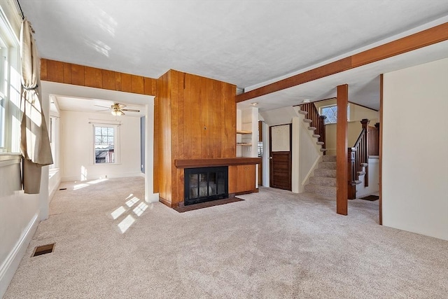 unfurnished living room with stairway, wooden walls, visible vents, and carpet flooring