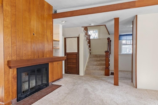 unfurnished living room with carpet, beam ceiling, a fireplace, and stairway