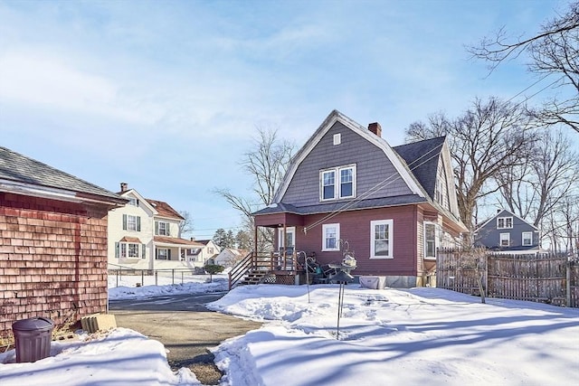 snow covered rear of property with a chimney, fence, and a gambrel roof