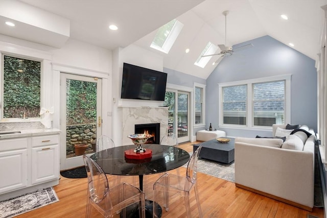 living area featuring a fireplace, light wood finished floors, a skylight, recessed lighting, and a ceiling fan