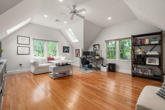 living room featuring a skylight, vaulted ceiling, light wood finished floors, a desk, and ceiling fan