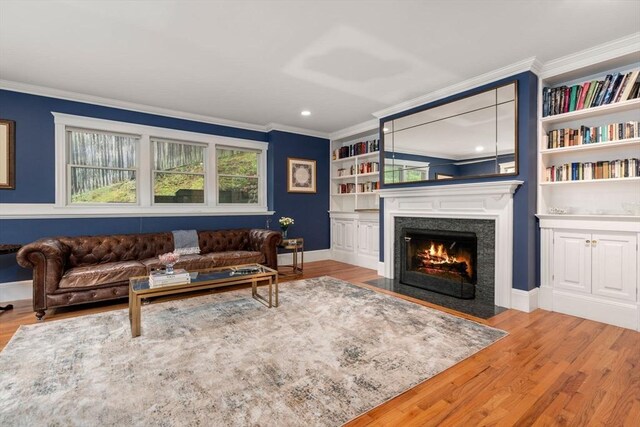 living area with wood finished floors, ornamental molding, a fireplace with flush hearth, baseboards, and recessed lighting