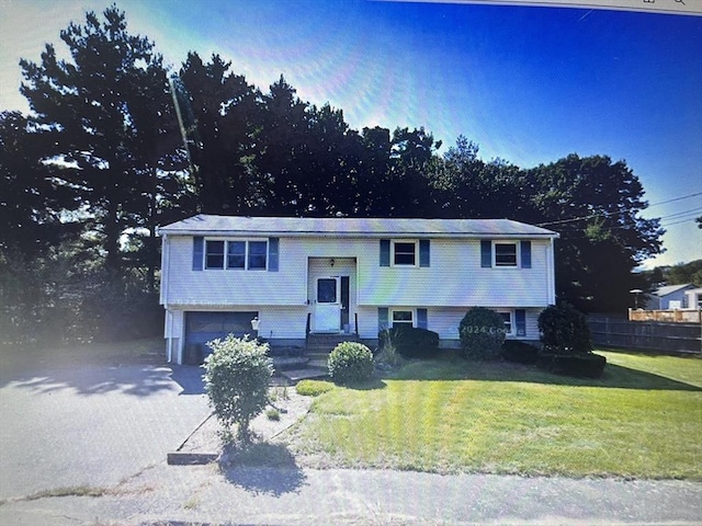 raised ranch featuring a front lawn, an attached garage, and driveway