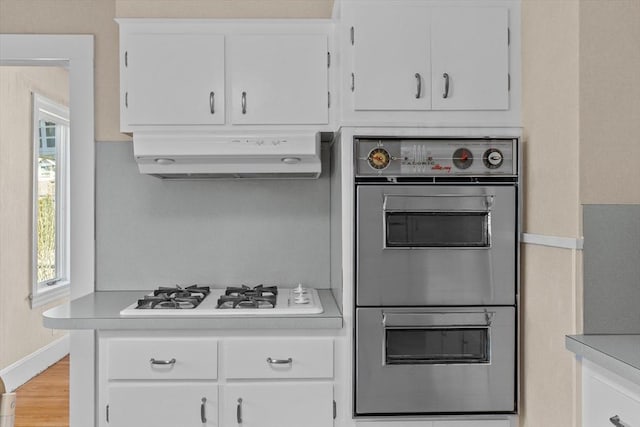 kitchen featuring double oven, light countertops, white cabinetry, white gas stovetop, and under cabinet range hood