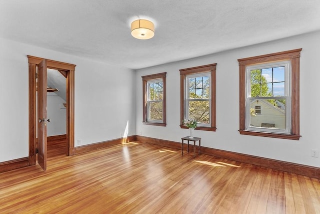 spare room featuring baseboards, a textured ceiling, and light wood-style flooring
