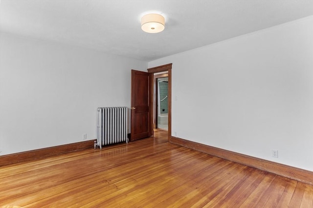empty room featuring baseboards, radiator, and light wood-style floors
