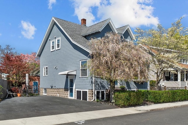 view of side of home with a shingled roof, fence, and a chimney