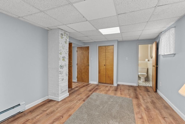 unfurnished bedroom with connected bathroom, a paneled ceiling, baseboards, wood finished floors, and a baseboard heating unit