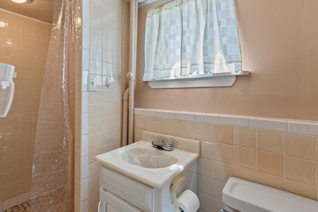 bathroom with vanity, a wainscoted wall, toilet, and tiled shower