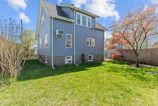 rear view of house featuring a lawn, a wall mounted AC, fence, and roof with shingles