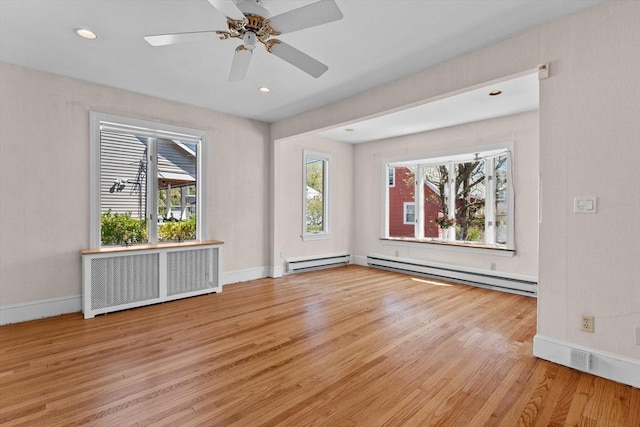 empty room with wood finished floors, plenty of natural light, and a baseboard heating unit