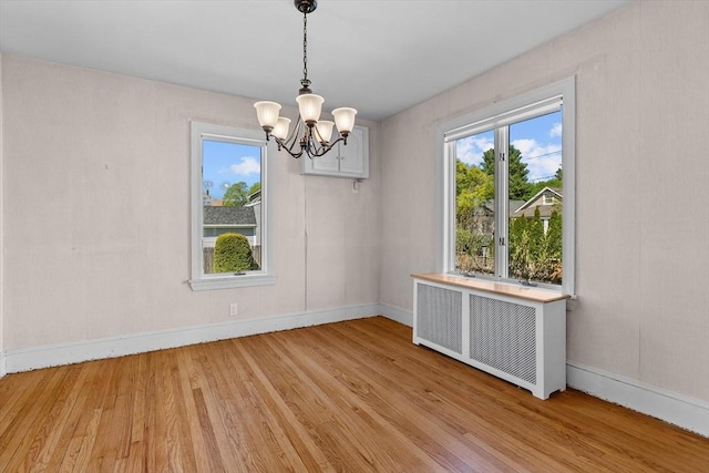 unfurnished dining area featuring baseboards, light wood-style flooring, radiator heating unit, and a notable chandelier