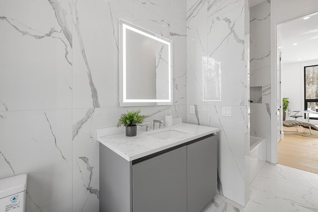 bathroom featuring marble finish floor, stone wall, toilet, and vanity