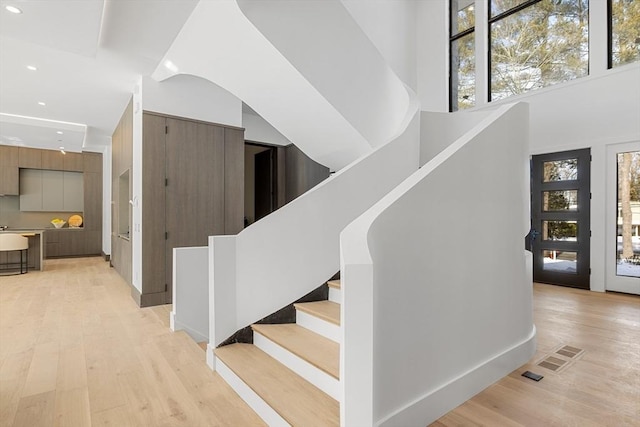 staircase with a towering ceiling, a wealth of natural light, and wood finished floors