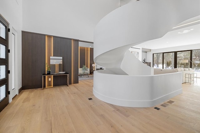 hall with light wood-type flooring, a towering ceiling, and visible vents