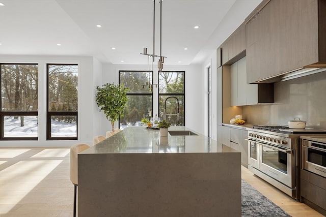 kitchen featuring plenty of natural light, range with two ovens, modern cabinets, decorative light fixtures, and a sink