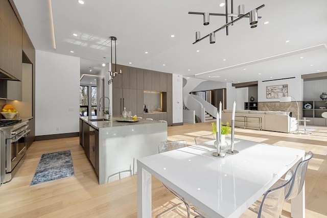 kitchen with decorative light fixtures, a sink, double oven range, modern cabinets, and a center island with sink