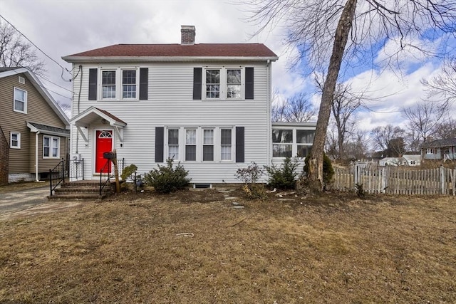 colonial house featuring a chimney, a sunroom, a front yard, and fence