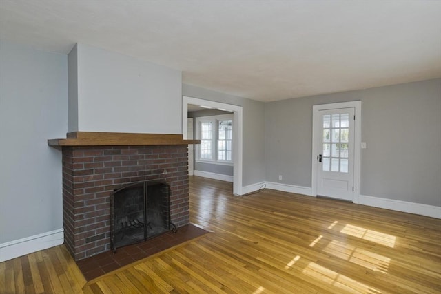 unfurnished living room featuring plenty of natural light, a fireplace, baseboards, and wood-type flooring