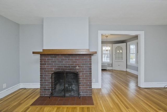 unfurnished living room with baseboards, radiator, a brick fireplace, and wood finished floors