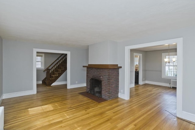 unfurnished living room featuring a wealth of natural light, light wood-style floors, a brick fireplace, and radiator heating unit