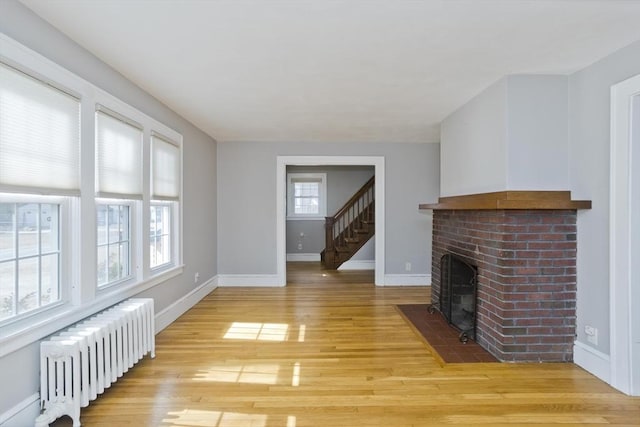 living area featuring radiator, light wood-type flooring, baseboards, and a brick fireplace