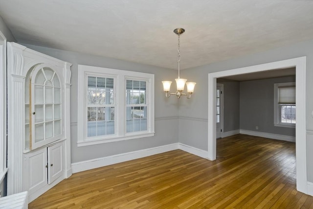 unfurnished dining area with hardwood / wood-style flooring, a notable chandelier, and baseboards