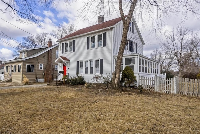 colonial home featuring a chimney, a sunroom, a front yard, and fence