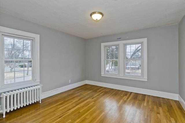 spare room with baseboards, wood-type flooring, and radiator heating unit