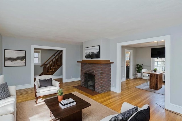 living room featuring stairway, baseboards, light wood-style flooring, and a fireplace