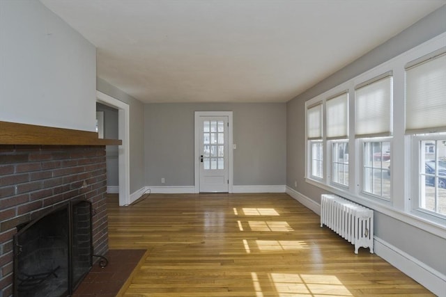 unfurnished living room featuring baseboards, wood finished floors, a fireplace, and radiator heating unit