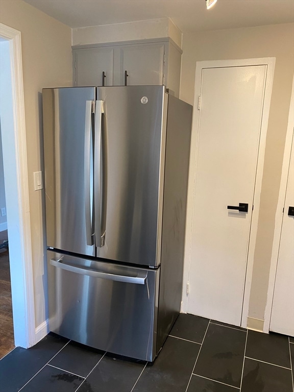 kitchen featuring dark tile patterned floors, white cabinets, and stainless steel fridge