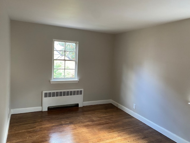 spare room with radiator heating unit and dark hardwood / wood-style floors