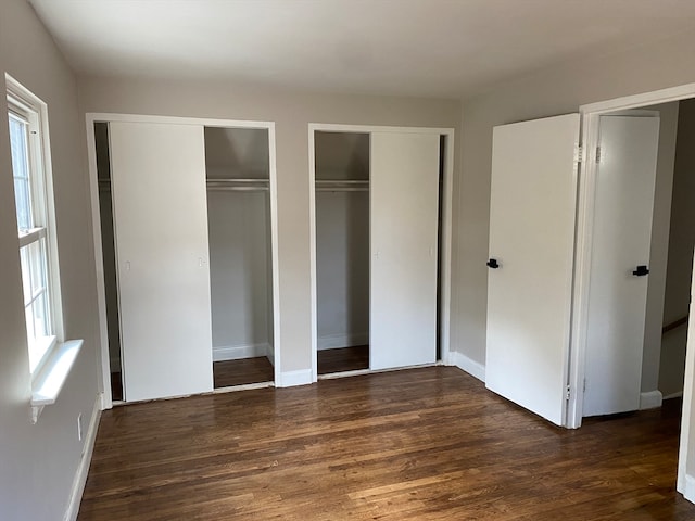 unfurnished bedroom with multiple windows, two closets, and dark hardwood / wood-style flooring