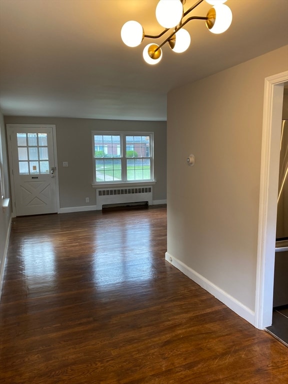 empty room with radiator heating unit, a chandelier, and dark wood-type flooring