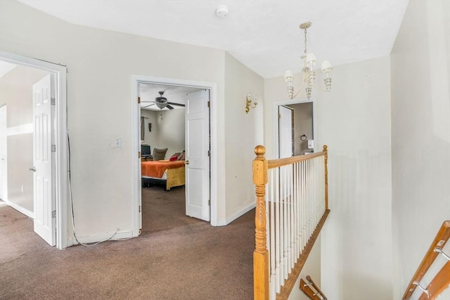 hall featuring a chandelier, dark colored carpet, an upstairs landing, and baseboards