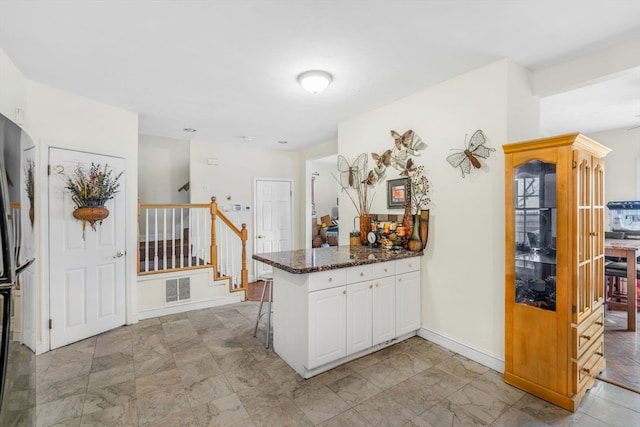 kitchen featuring white cabinetry, kitchen peninsula, dark stone counters, and light tile patterned floors