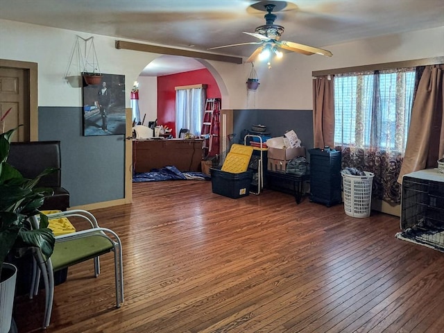 living room featuring a healthy amount of sunlight, wood-type flooring, arched walkways, and a ceiling fan