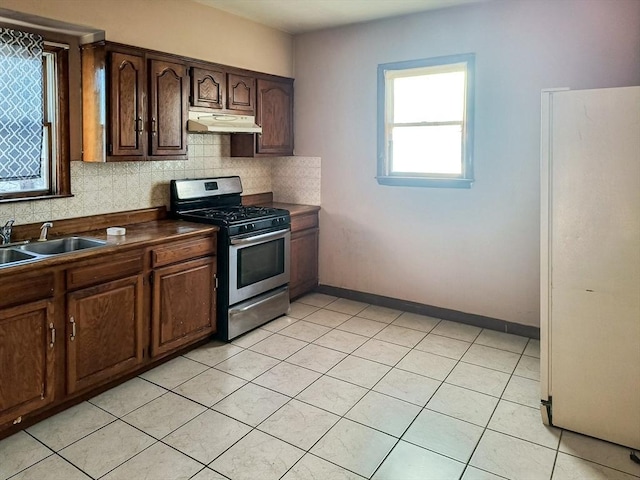 kitchen featuring dark countertops, freestanding refrigerator, a sink, stainless steel gas range, and under cabinet range hood