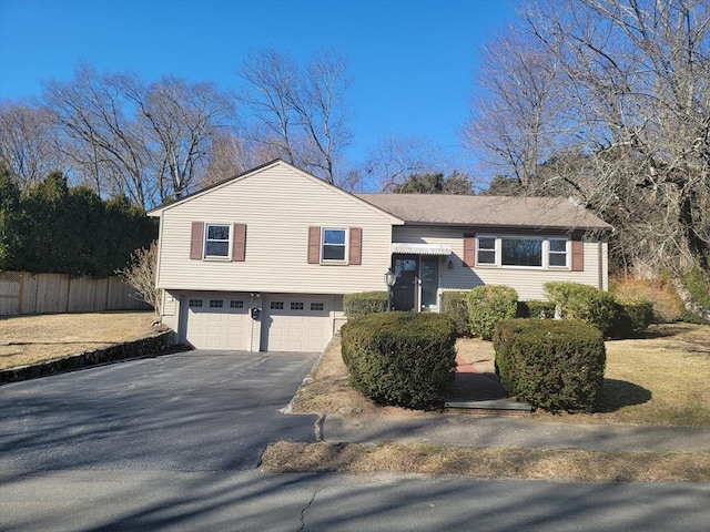 raised ranch with an attached garage, driveway, and fence