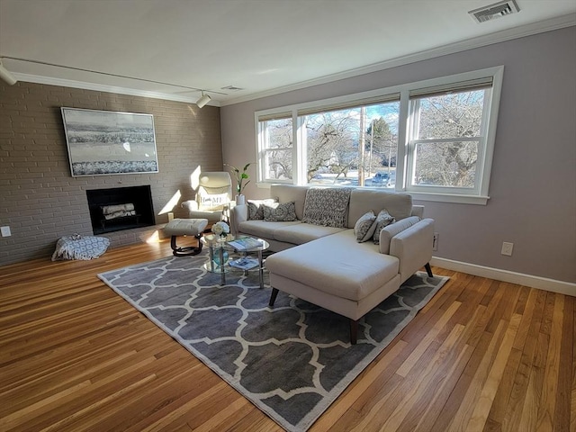 living area with visible vents, a fireplace, wood finished floors, and ornamental molding