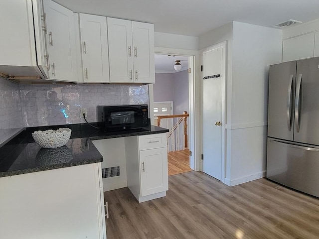 kitchen featuring dark stone countertops, visible vents, freestanding refrigerator, white cabinets, and light wood-style floors