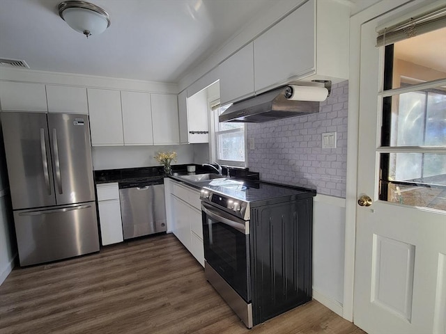 kitchen with a sink, stainless steel appliances, under cabinet range hood, white cabinetry, and dark countertops