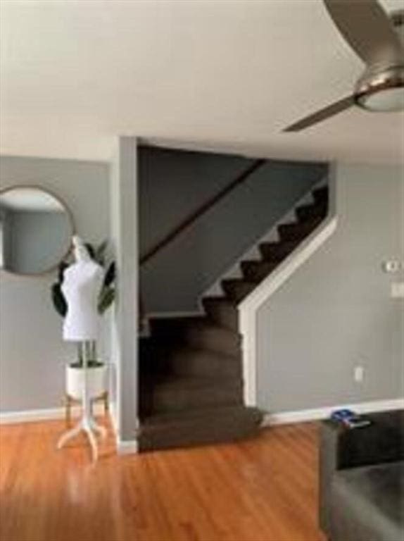 staircase with wood finished floors, ceiling fan, and baseboards
