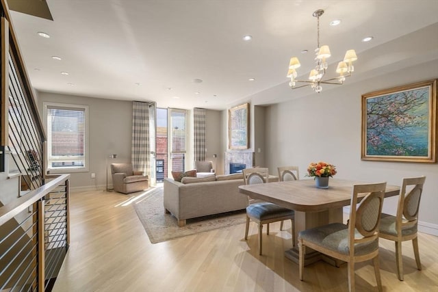 dining room with an inviting chandelier, light wood-style flooring, baseboards, a glass covered fireplace, and recessed lighting